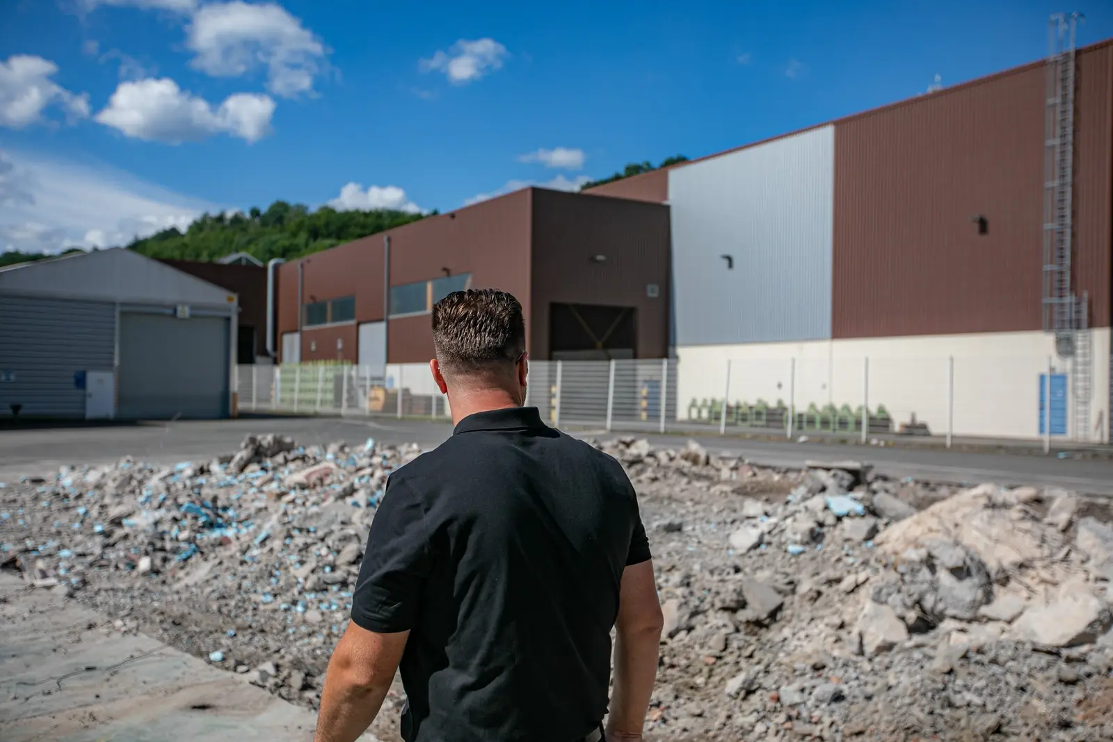 Mitarbeiter vor dem Bruchmaterial einer Industriefläche, dahinter Fabrik- und Lagerhallen
