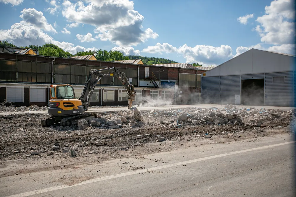 Bagger stemmt Betonflächen vor einer Industriehalle auf