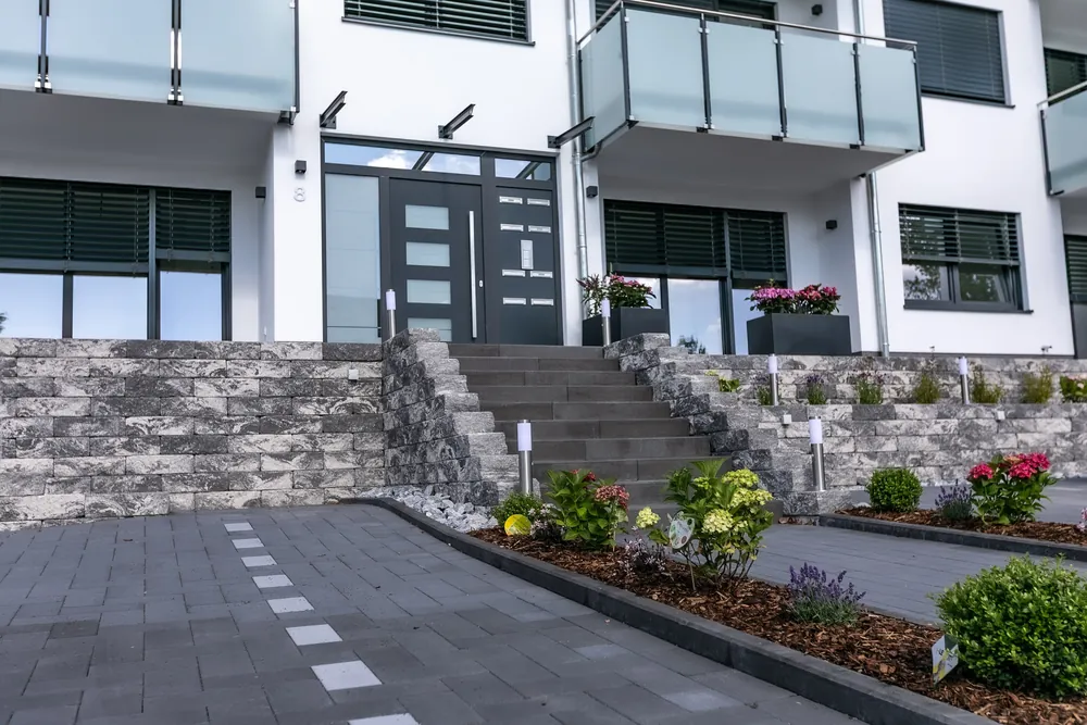 Hauseingang mit Blockstufentreppe, Beeten und Pollerleuchten an einem Mehrfamilienhaus
