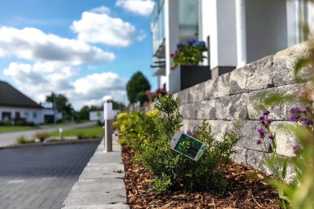 Frisch bepflanztes Beet mit Rindenmulch vor einer Mauer aus Mauersteinen