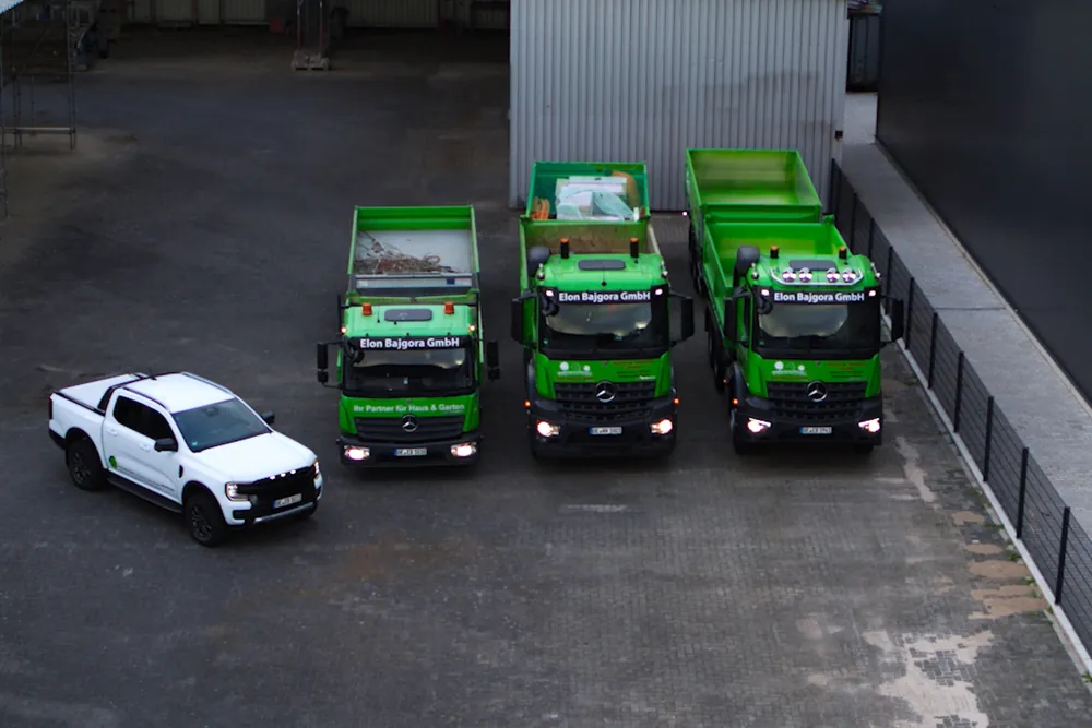 Drohnenaufnahme: drei grüne Mercedes-Kipper der Elon Bajgora GmbH und ein weißer Pick-up auf dem Betriebshof