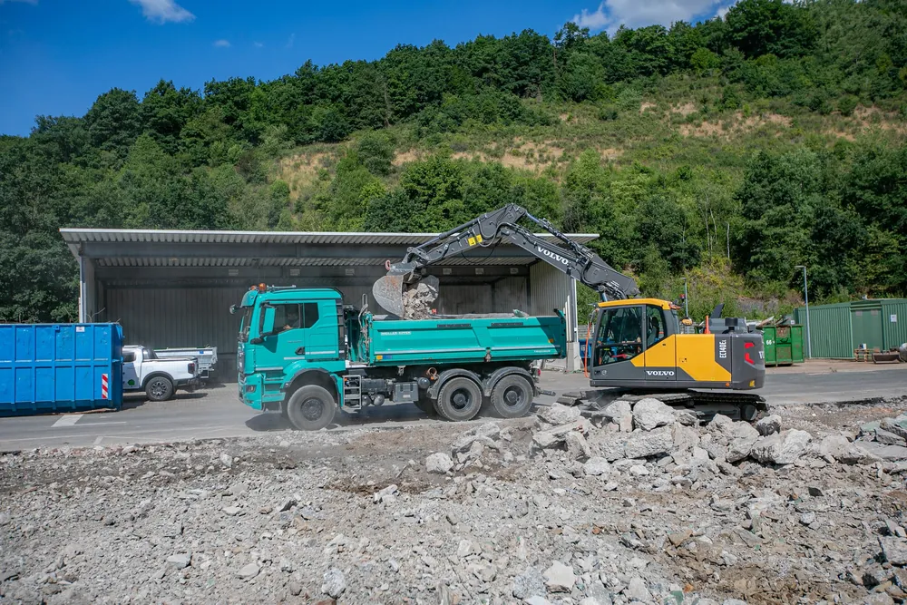Bagger belädt einen Dreiseitenkipper mit Abbruchmaterial